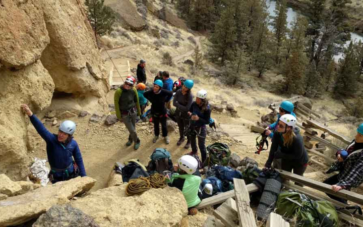 an outward bound instructor points at a rock while while a group of adults wearing helmets observe